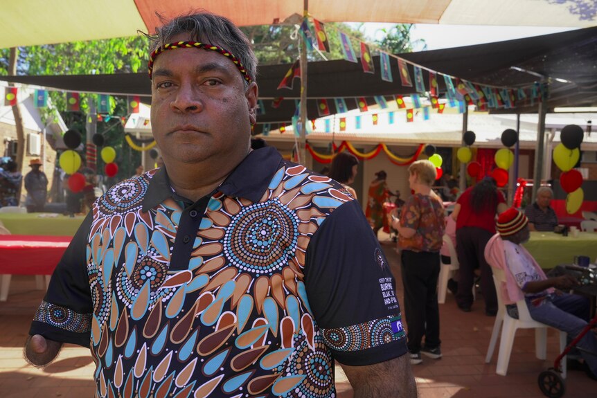 A photo showing an Indigenous man wearing a polo shirt with Indigenous art looking directly at the camera.