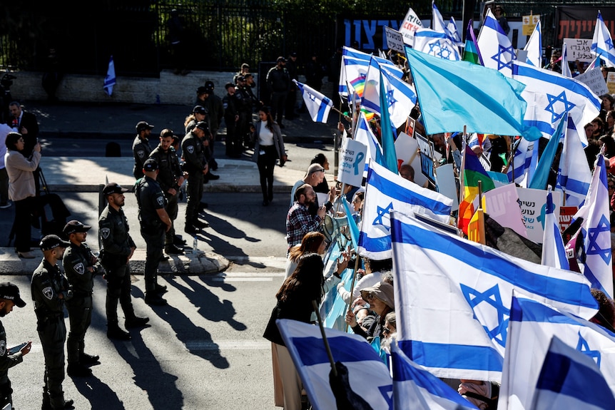 Protesters seen holding signs as flags opposite Israeli security force members.