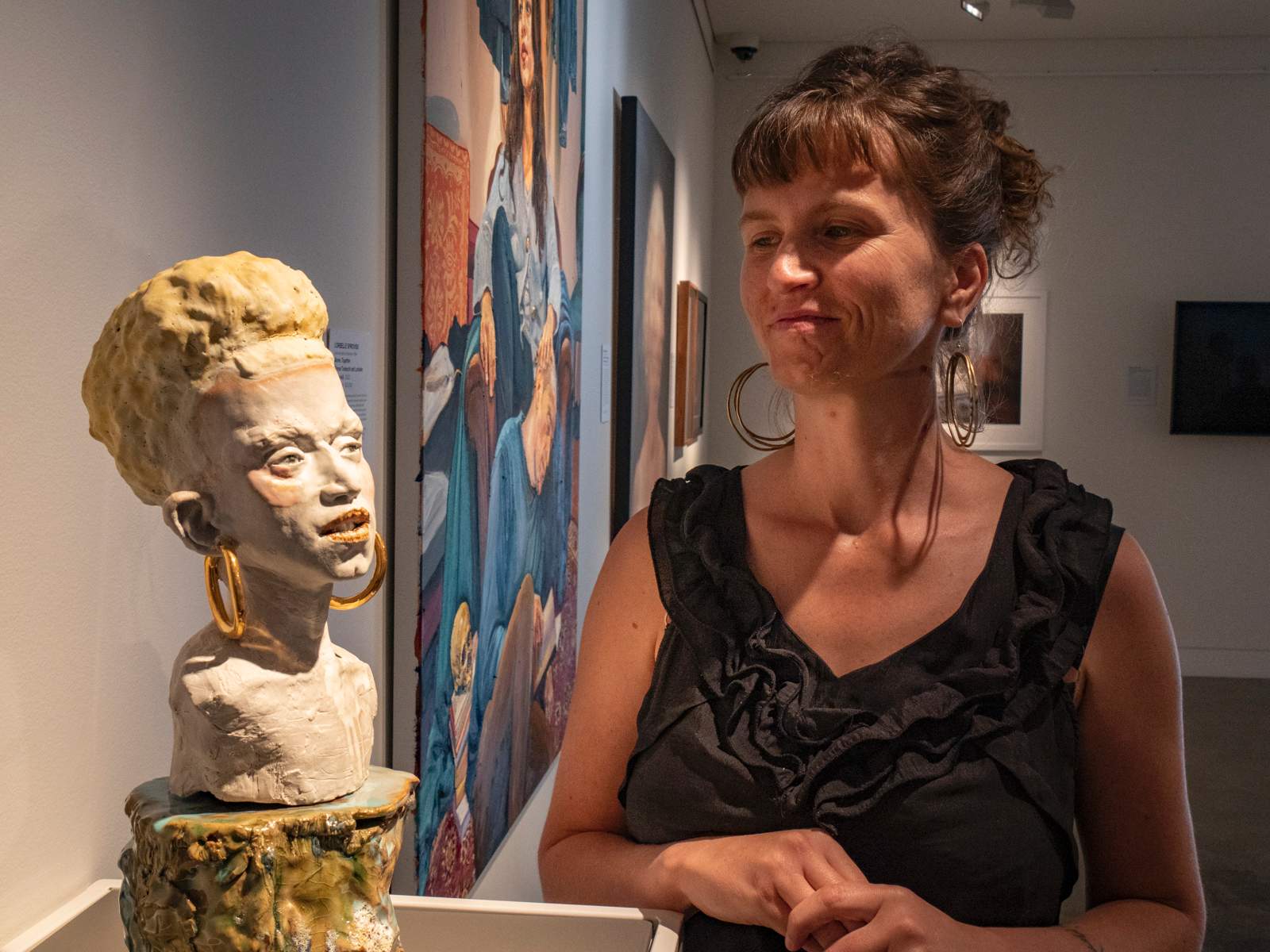 A ceramic bust of a woman on left and a woman standing on right looking at it.