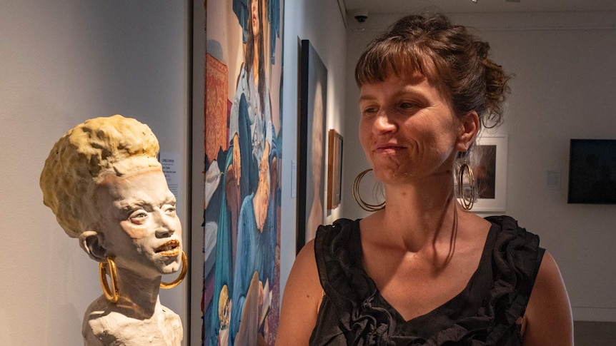 A ceramic bust of a woman on left and a woman standing on right looking at it.