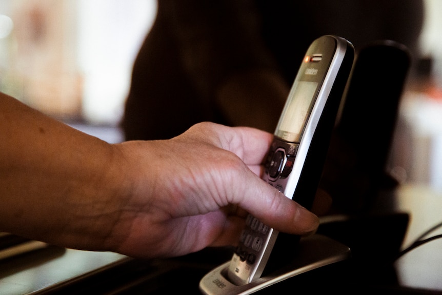 Denise's hand reaches for a black cordless landline phone.