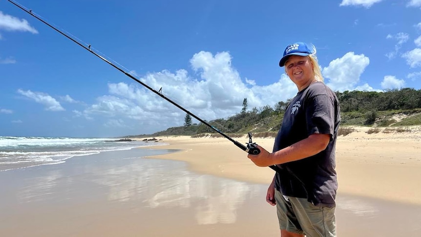 Boy on beach with fishing rod smiling at camera.