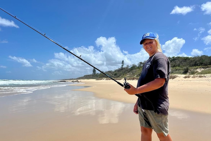 Boy on beach with fishing rod smiling at camera