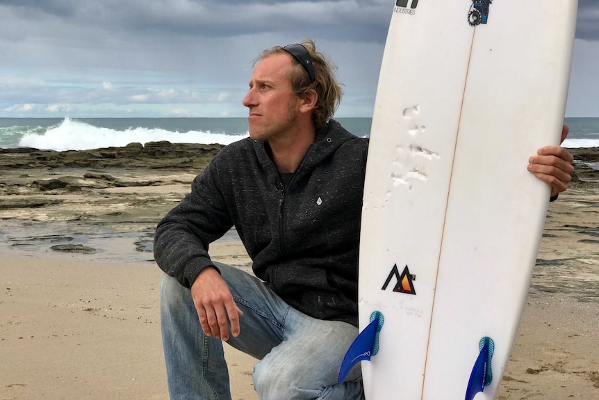 Surfer Marcel Brundler with his damaged surfboard on the beach.