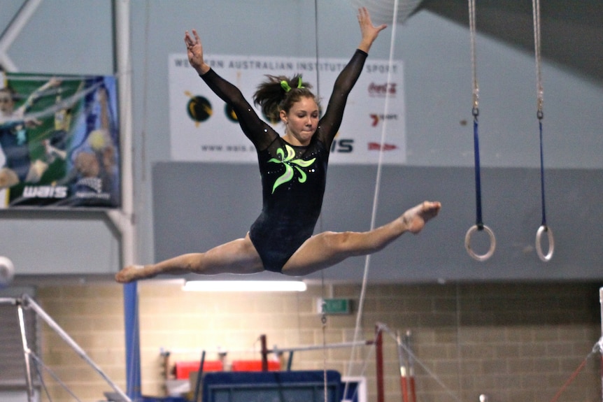 A gymnast does mid-air splits in a gymnasium.