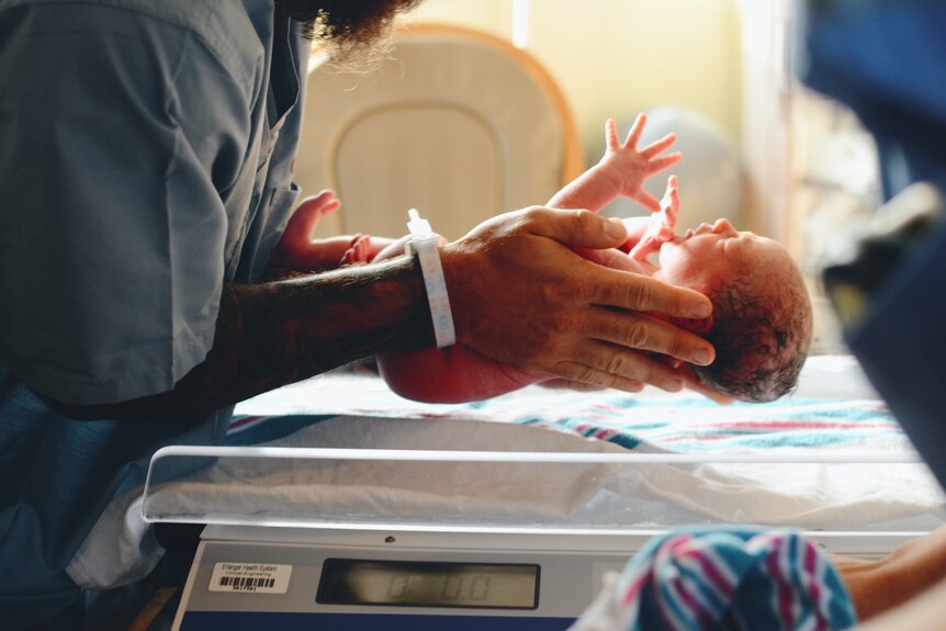 A newborn baby is cradled in a hospital.