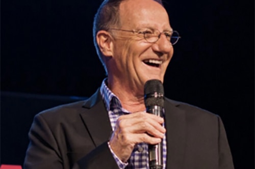 a man in a collared shirt and blazer holding a microphone and smiling