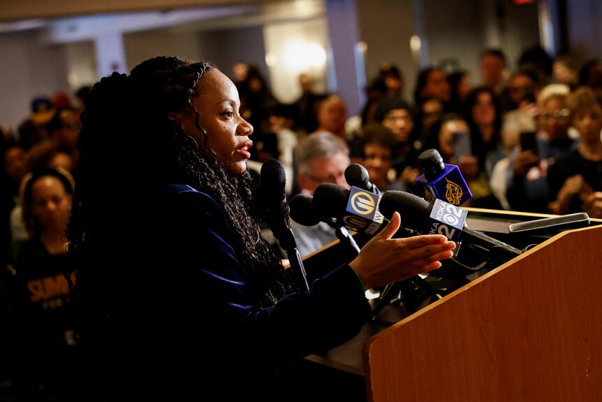 A black woman speaks at a podium in front of a crowd 