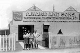 A historic photo of four people standing outside a Gladstone shed. 