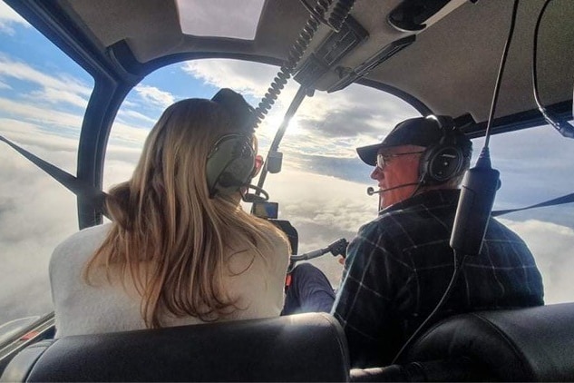 a couple in a helicopter looking over the clouds in the sky
