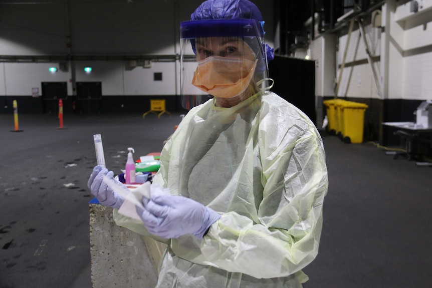 Cheryl wears all of her personal protective equipment, so you can only see her eyes. She holds a swab.