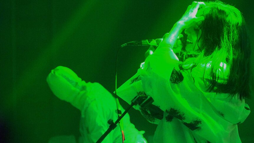 A woman holding a  microphone under green stage lights
