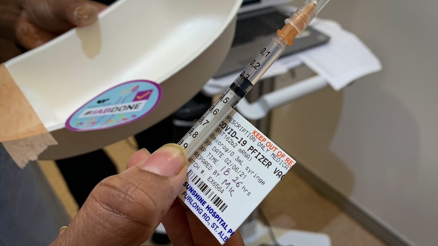 A hand holds a syringe labeled Covid-19 Pfizer.