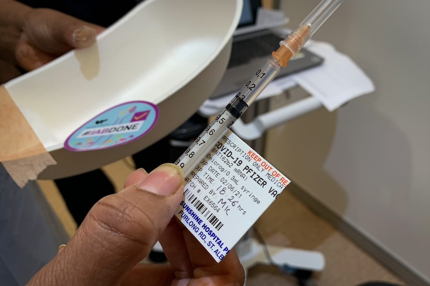 A hand holds a syringe labeled Covid-19 Pfizer.