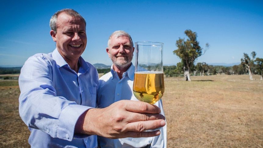 Two men standing in a paddock holding a glass of beer.