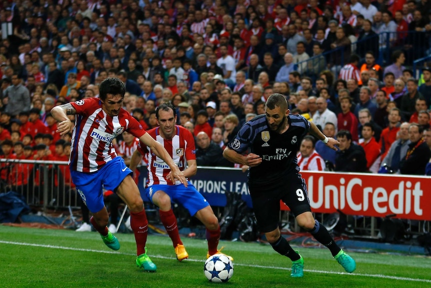 Real Madrid's Karim Benzema (R), has the ball as Atletico Madrid defenders try to stop him.
