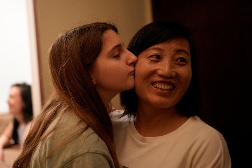 A girl with long brown hair leans over to kiss a Chinese woman with short, dark hair.