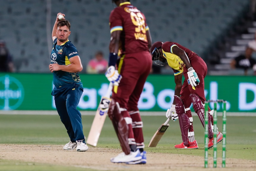 Marcus Stoinis with his arm lifted about to bowl a cricket ball, a man in front with a bat. 
