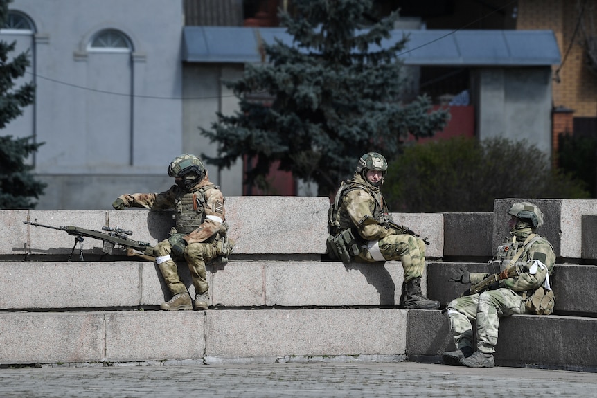 Three uniformed soldiers sit, reclining on wide concrete stairs at a plaza