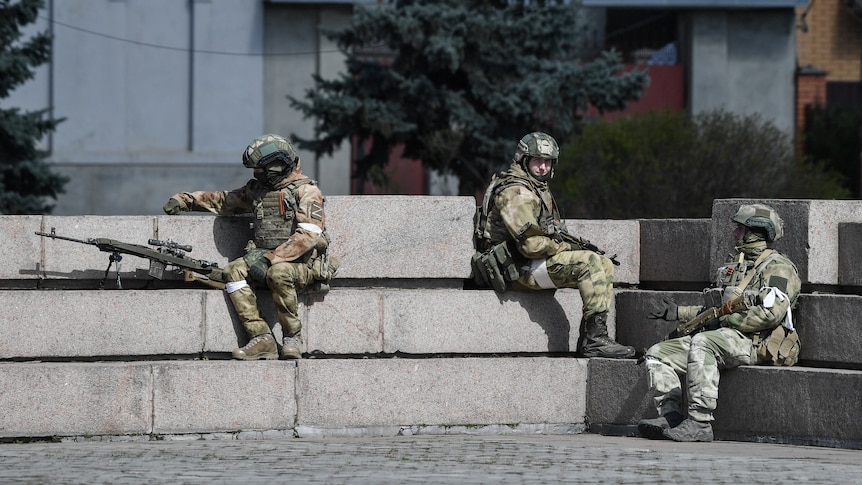 Three uniformed soldiers sit, reclining on wide concrete stairs at a plaza