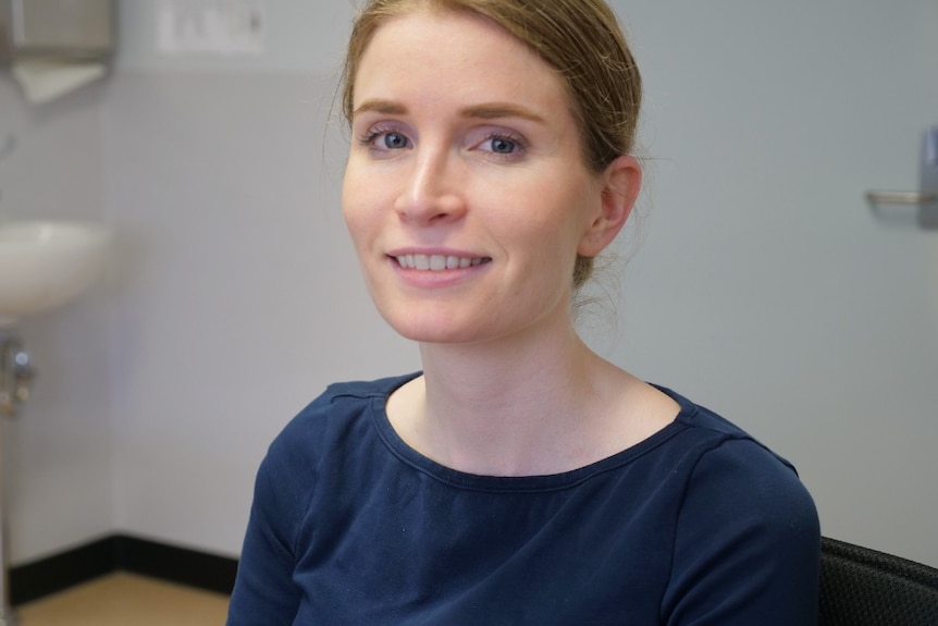 Liz Clarkson smiles at the camera, blue eyes, light brown hair, navy shirt, clinic in background.