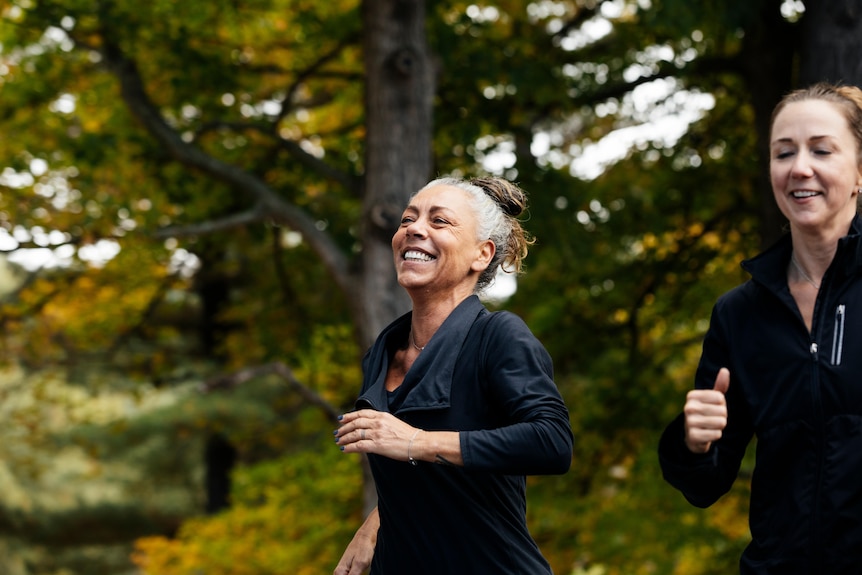 An older woman is running in the forest, smiling. 