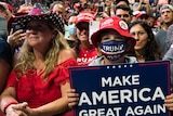 Boy in red hat, wearing blue mask holds sign reading 'make America great again'