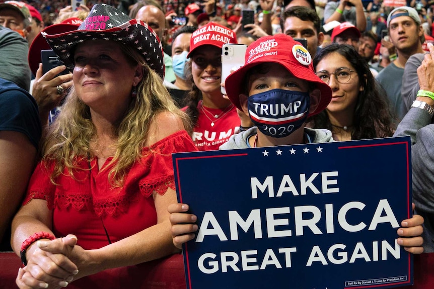 Boy in red hat, wearing blue mask holds sign reading 'make America great again'