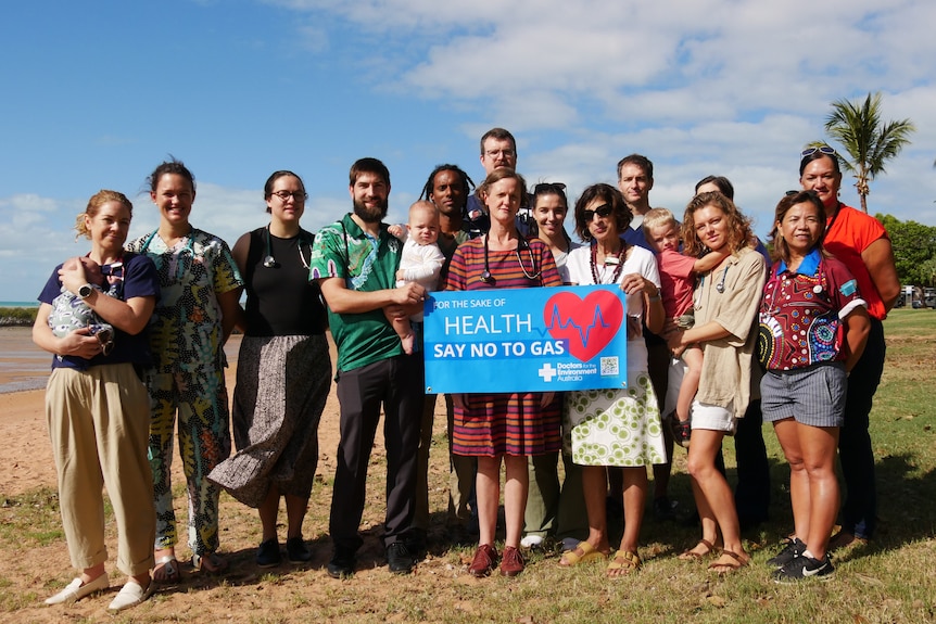 A group of people standing together on a beach holding a sign which says "health say no to gas".