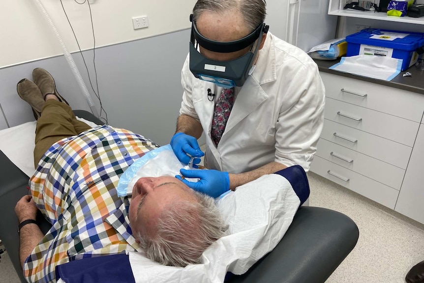 Doctor wearing mask and headlamp injects a man's face