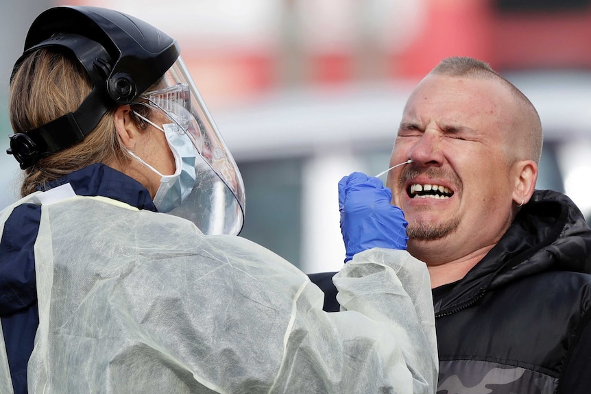 A man grimacing while a health worker in PPE sticks a swab up his nose