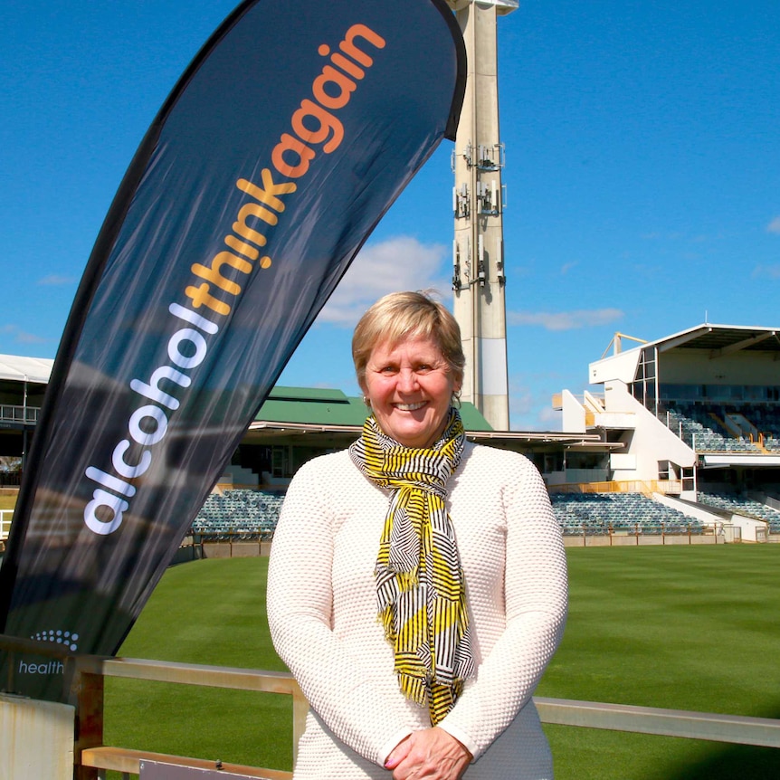 A woman standing in front of a sign that says Alcohol Think Again at a sporting stadium