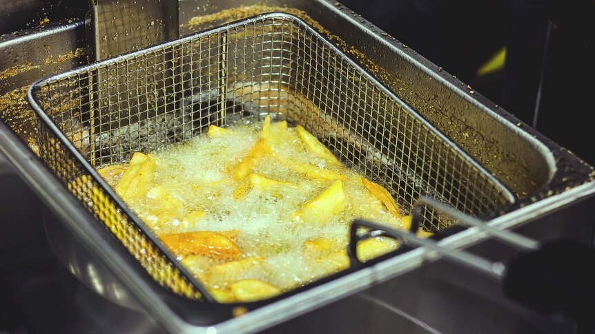 Thick cut chips sinking into glistening, bubbling oil in deep fryer