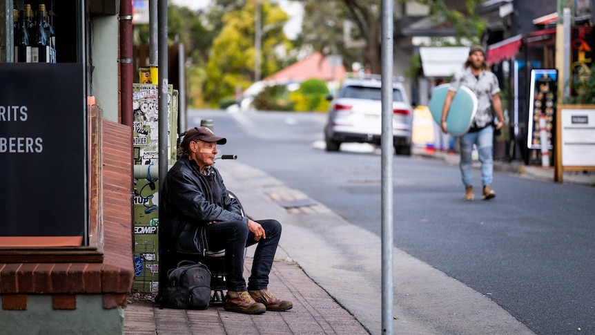 A man sits on the footpath in Byron Bay.