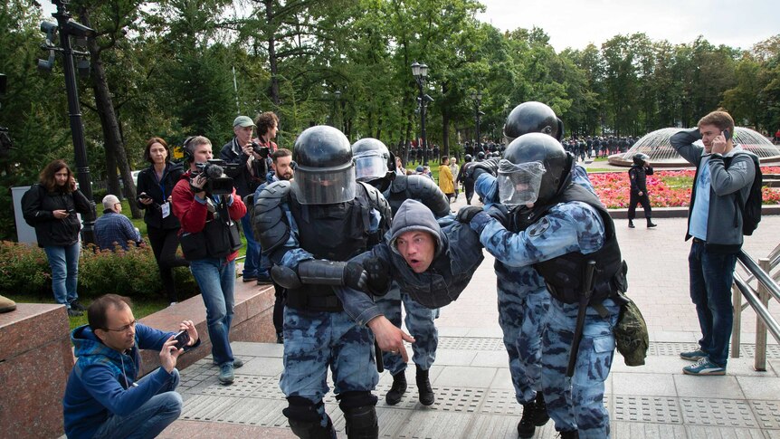 Police officers detain a protestor, lifting him off the ground as she shouts.