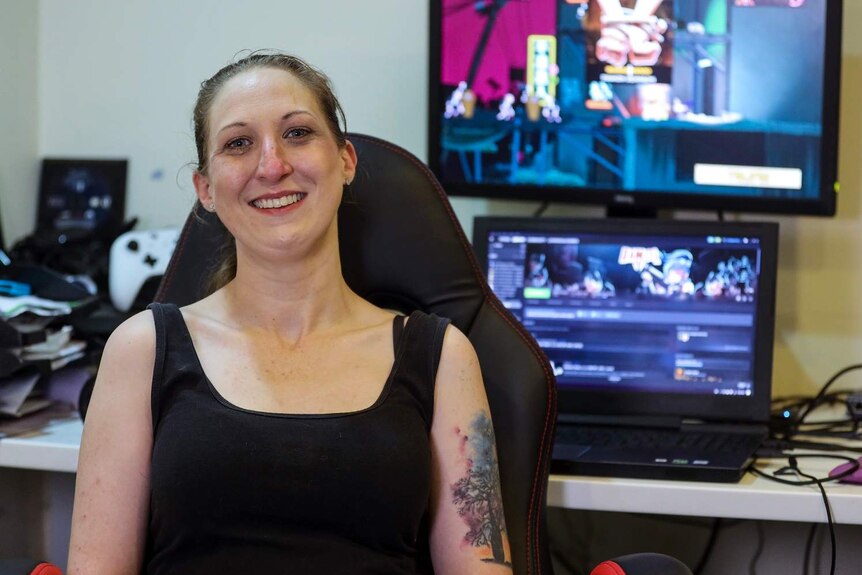 Megan Summers from Screwtape Studios sits in her home office in front of a video game played behind her