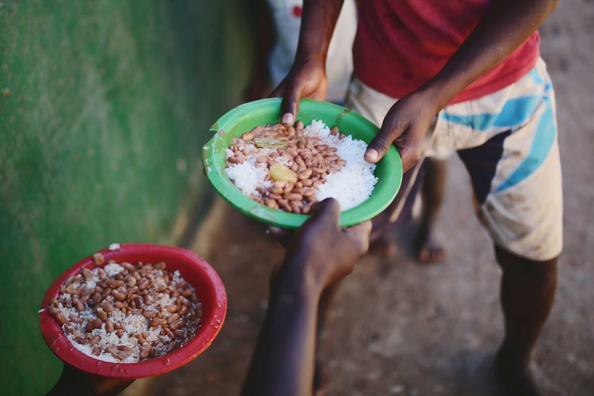 Rice and beans in plastic bowls being handed to children whose hands are seen taking them