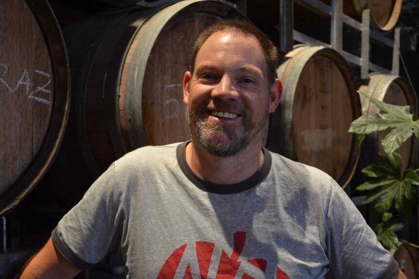 A smiling man standing in front of some wine barrels.