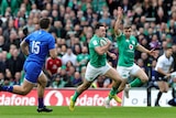 An Irish rugby union player runs past a French defender to score a try as his teammate raises his arm in celebration.