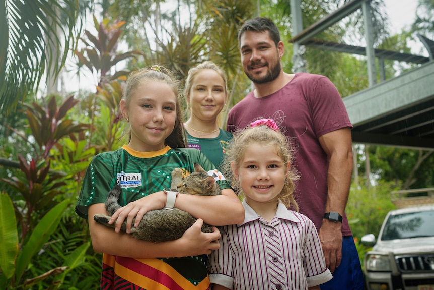 Lennair and Aidan Hill smile to the camera with daughters Lakhyah and Natayah. Their eldest daughter is holding a small cat.