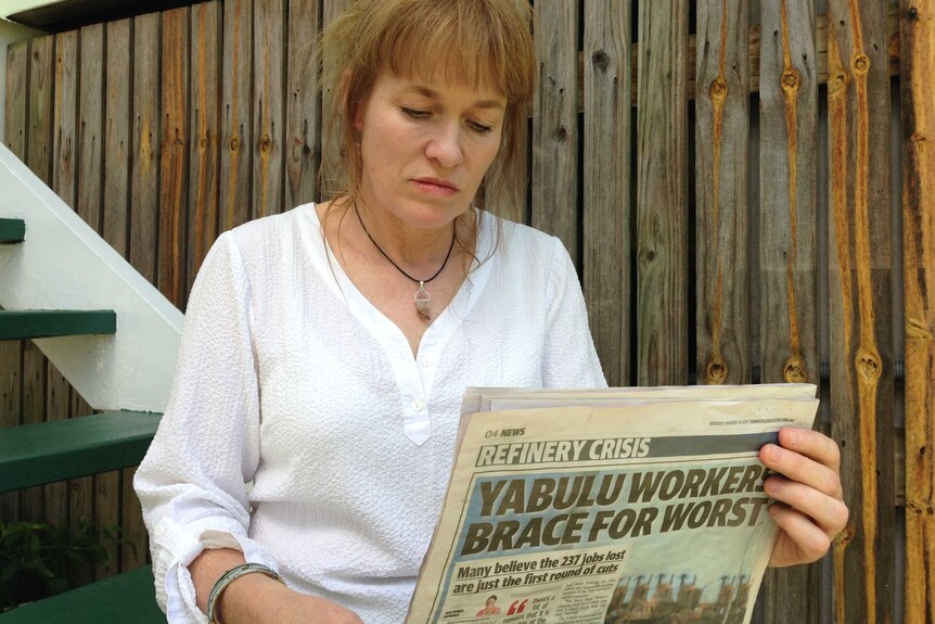 Sam Larkins reads a newspaper showing the headline 'yabulu workers brace for worst'.