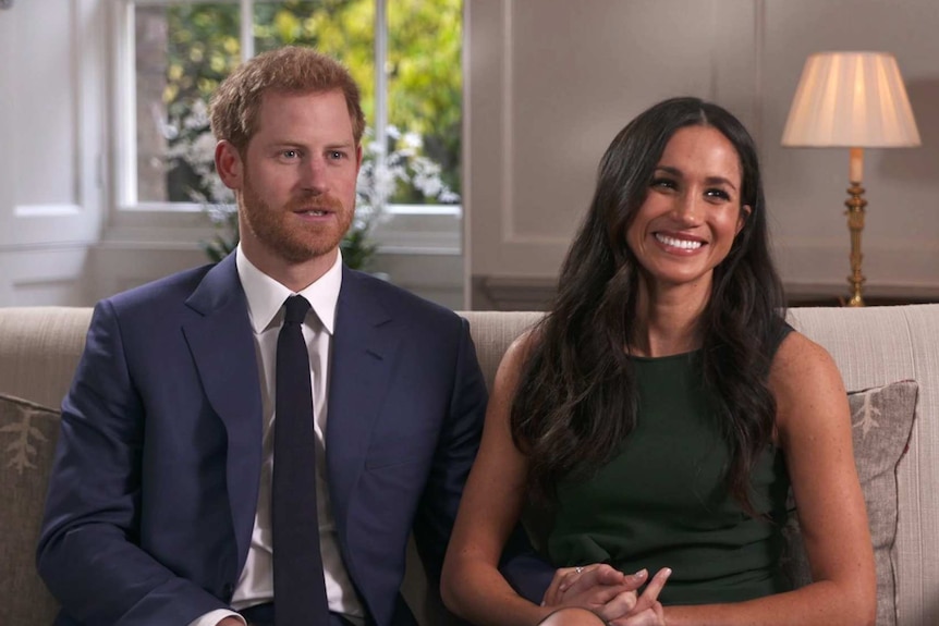 Britain's Prince Harry and Meghan Markle sit next to each other on a couch holding hands in an interview about their engagement.