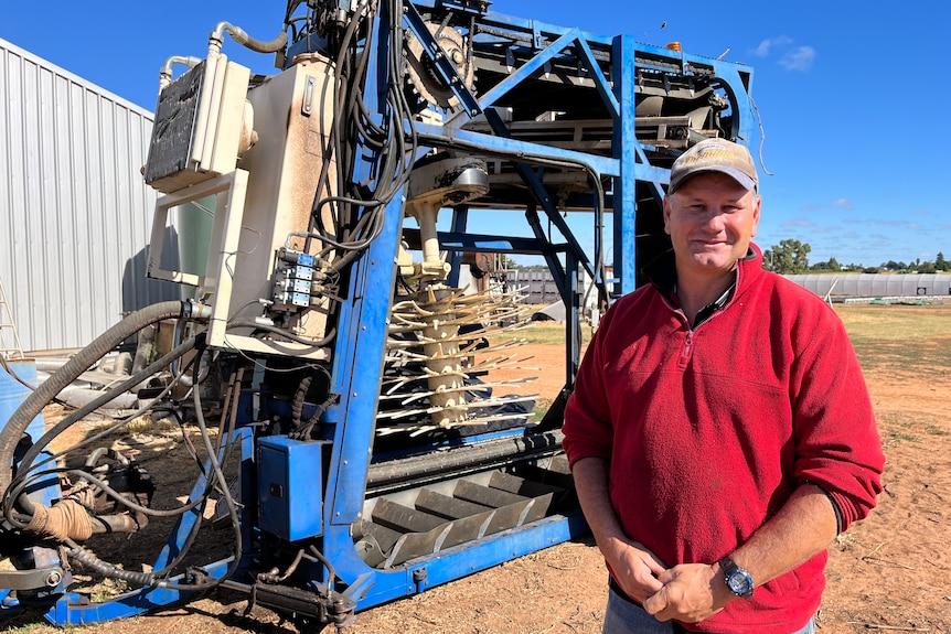 Ashley Johnstone stands in front of his dried fruit harvester. The machine is towed by a tractor