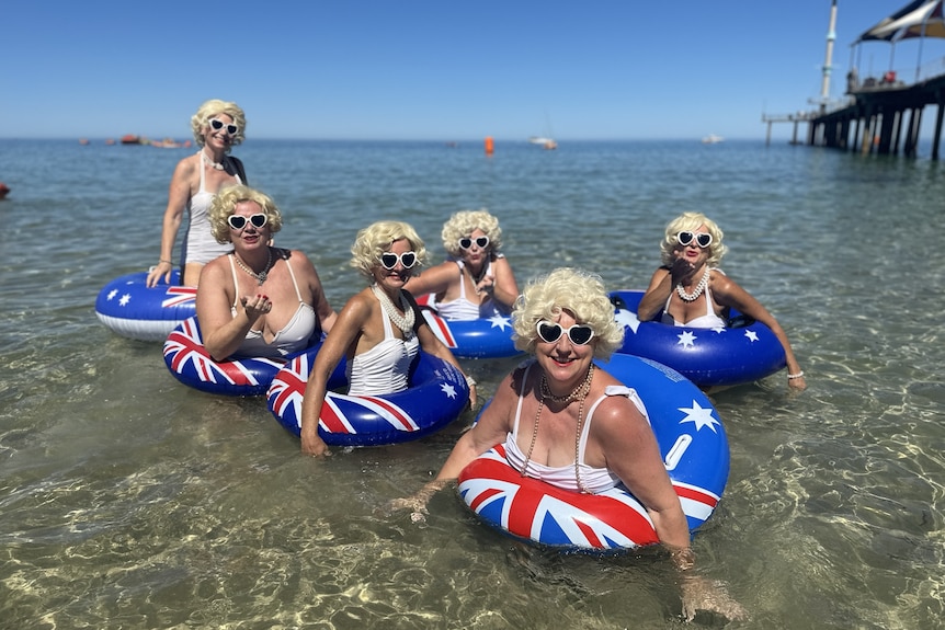 Six women dressed as Marilyn Monroe with blue floaties in the water.