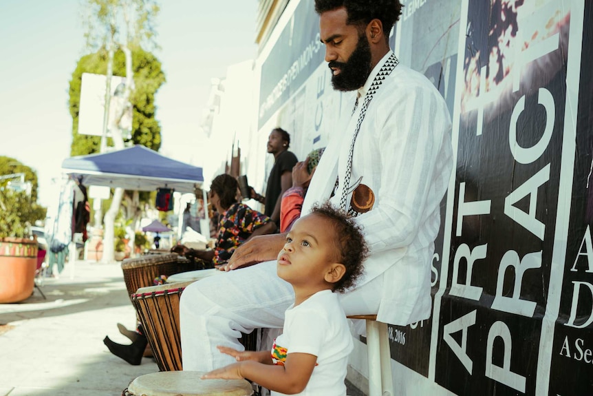 A man and his son play a drum.