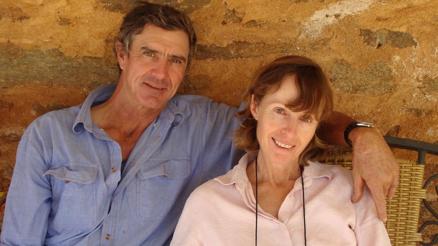 A man and women sit against a rock wall and smile at the camera