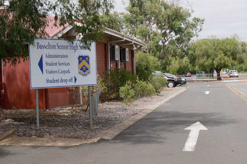 A sign outside of Busselton Senior High School with a building and trees in the background.