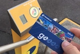 Commuter holding a blue Go Card in front of a "tap on" station.