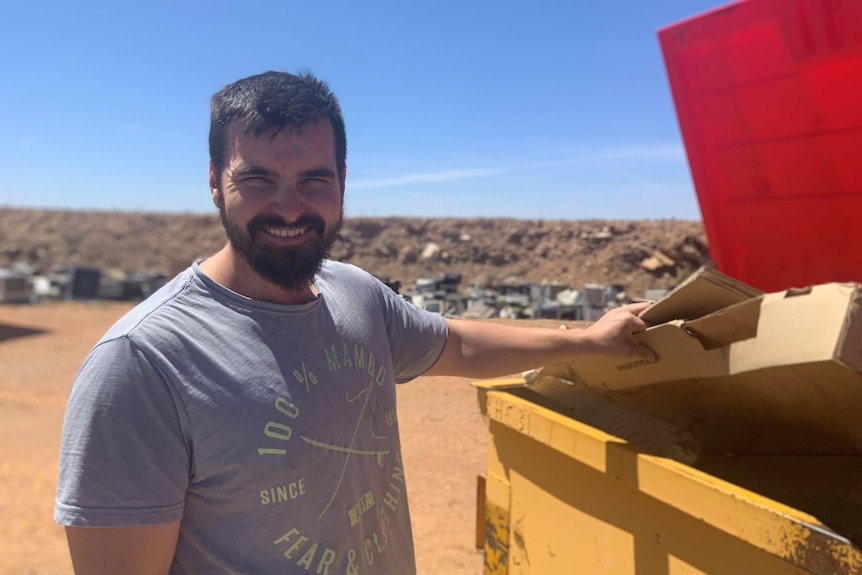 Joe O'Connor smiling next to a recycling skip bin for paper and cardboard