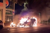 A parked car on fire with flames and smoke coming out late at night in France
